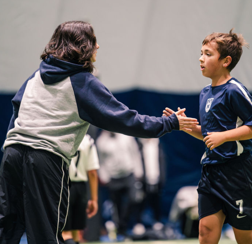 Coach high-fiving a Maravilha rep player during indoor training